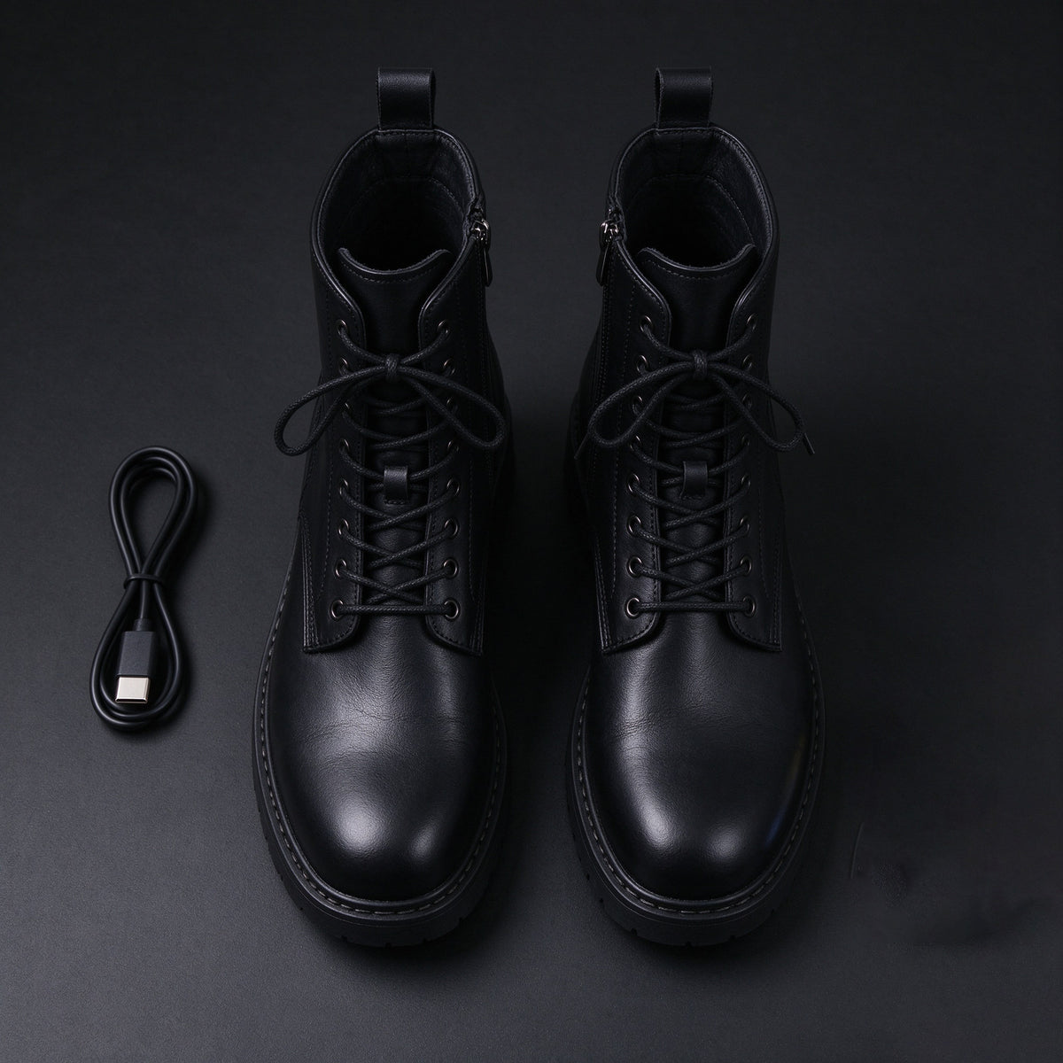 Pair of black leather electric combat boots with a charging cable on a dark background